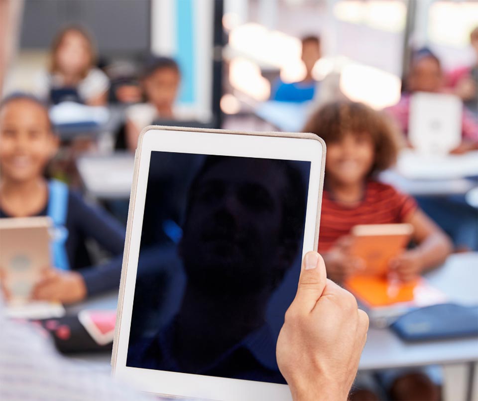 Lehrer steht mit iPad in der Hand vor der Klasse